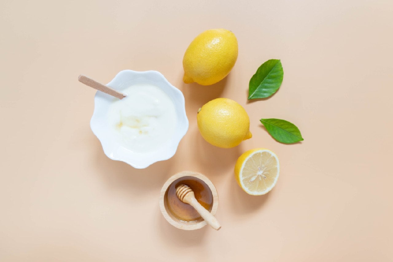 Ingredientes para incrementar a limonada suíça: limões, mel, creme de leite e folhas verdes dispostos sobre fundo claro.