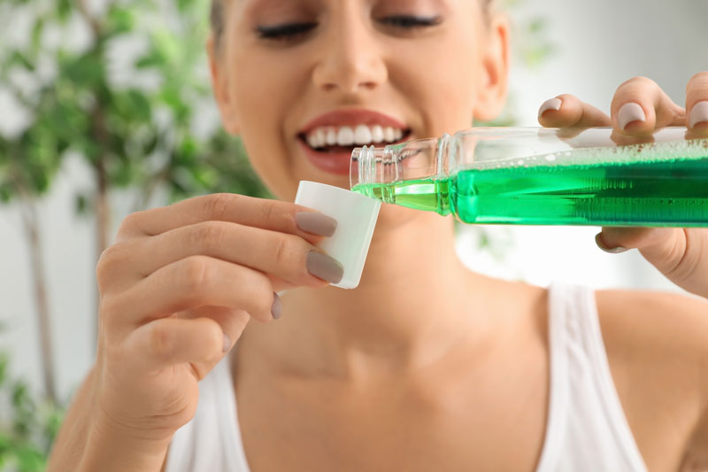 Mulher usando um enxaguante bucal depois da escovação para não precisar de uma bala de hortelã depois