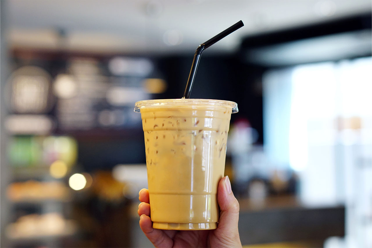 Imagem de uma mão segurando um copo de café gelado em uma cafeteria