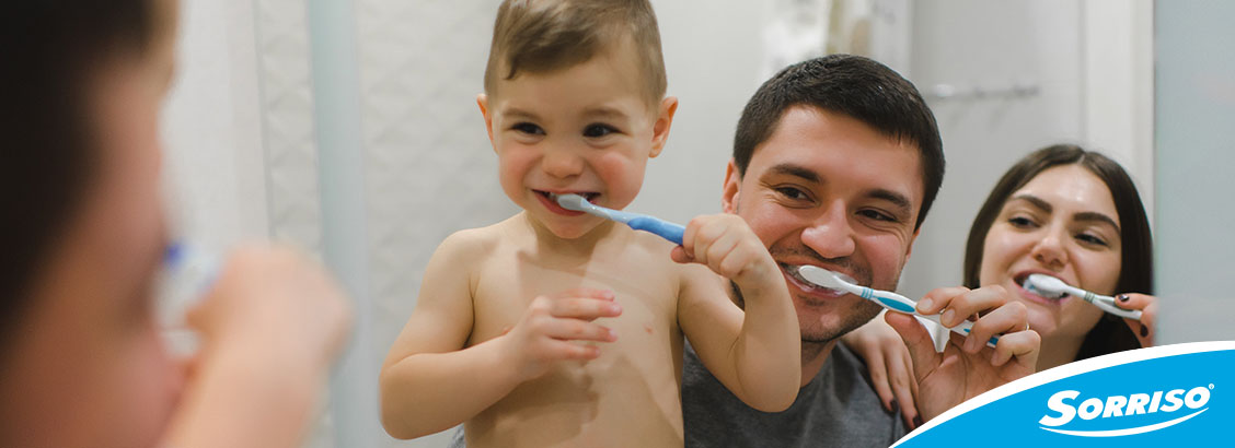 criança pequena com os pais em frente ao espelho para que ele aprenda como escovar os dentes