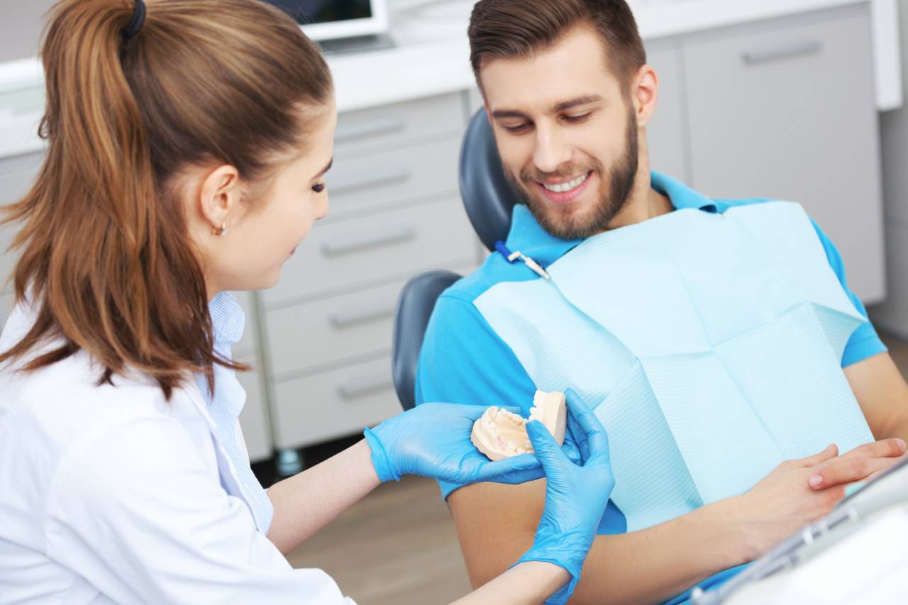 Dentista usando um molde de arcada dentária como exemplo para explicar para o paciente como evitar tártaro.