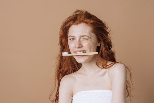 Moça ruiva segurando escova com os dentes pronta para arrasar escovando os dentes com creme dental Sorriso após sair do banho