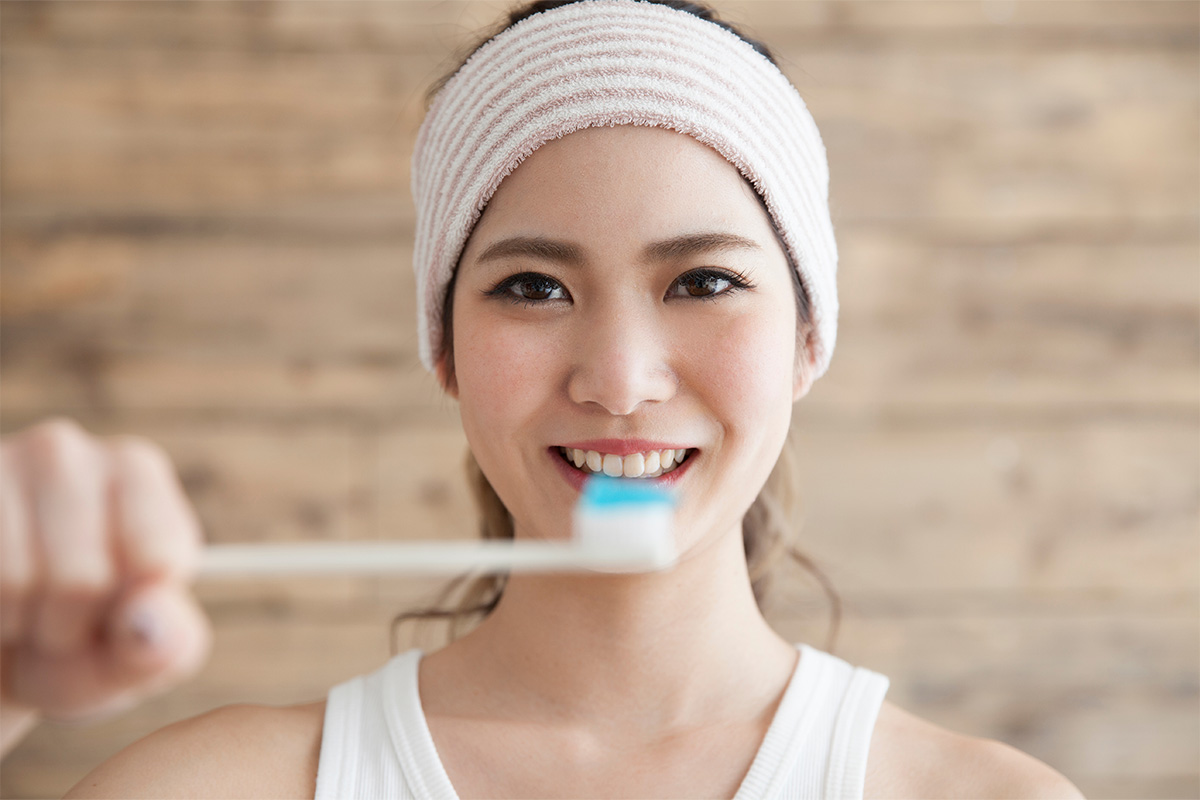 Mulher sorridente segurando uma escova de dentes branca com gel dental azul em frente ao rosto Mulher sorridente segurando uma escova de dentes branca com gel dental azul em frente ao rosto
