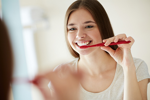 Mulher jovem sorrindo enquanto escova os dentes com uma escova de dentes vermelha e pasta de dente para cárie. Mulher jovem sorrindo enquanto escova os dentes com uma escova de dentes vermelha e pasta de dente para cárie.